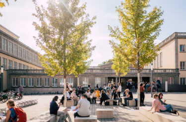 Teilnehmende sitzen in der Sonne im Innenhof vor dem Tagungsgebäude