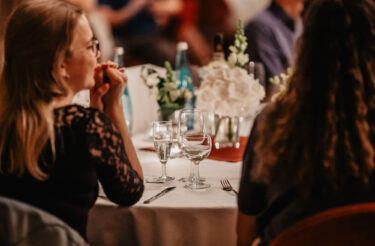 Zwei Personen sitzen bei einem festlich gedeckten Tisch mit Gläsern und Blumen