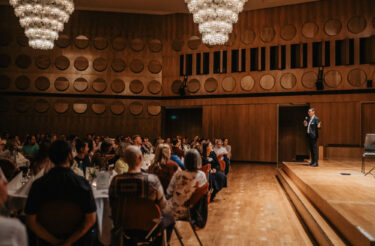 Redner spricht auf der Bühne vor sitzendem Publikum im großen Festsaal