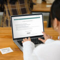Teilnehmerin startet eine digitale Prüfung mit evaexam auf dem Laptop, TAN-Code liegt als Papierkarte daneben