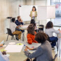 Personen in einem modernen Seminarraum bei einer Gruppenarbeitsphase, eine Referentin steht vor dem Flipchart