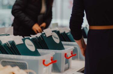 Das evasys-Team heißt die Teilnehmenden am Check-in willkommen und verteilt Tagungsunterlagen. Das Bild steht für Organisation und Gastfreundschaft.