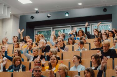 Teilnehmende heben im Hörsaal die Hand während einer Fragerunde