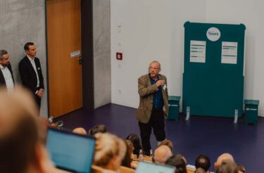 Referent spricht mit Mikrofon vor dem Publikum im Hörsaal