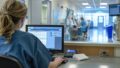 Pflegekraft arbeitet am Computer am Empfang einer Klinikstation
