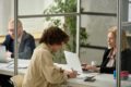 Person filling out a citicen survey at a public service desk while staff members provide administrative support.